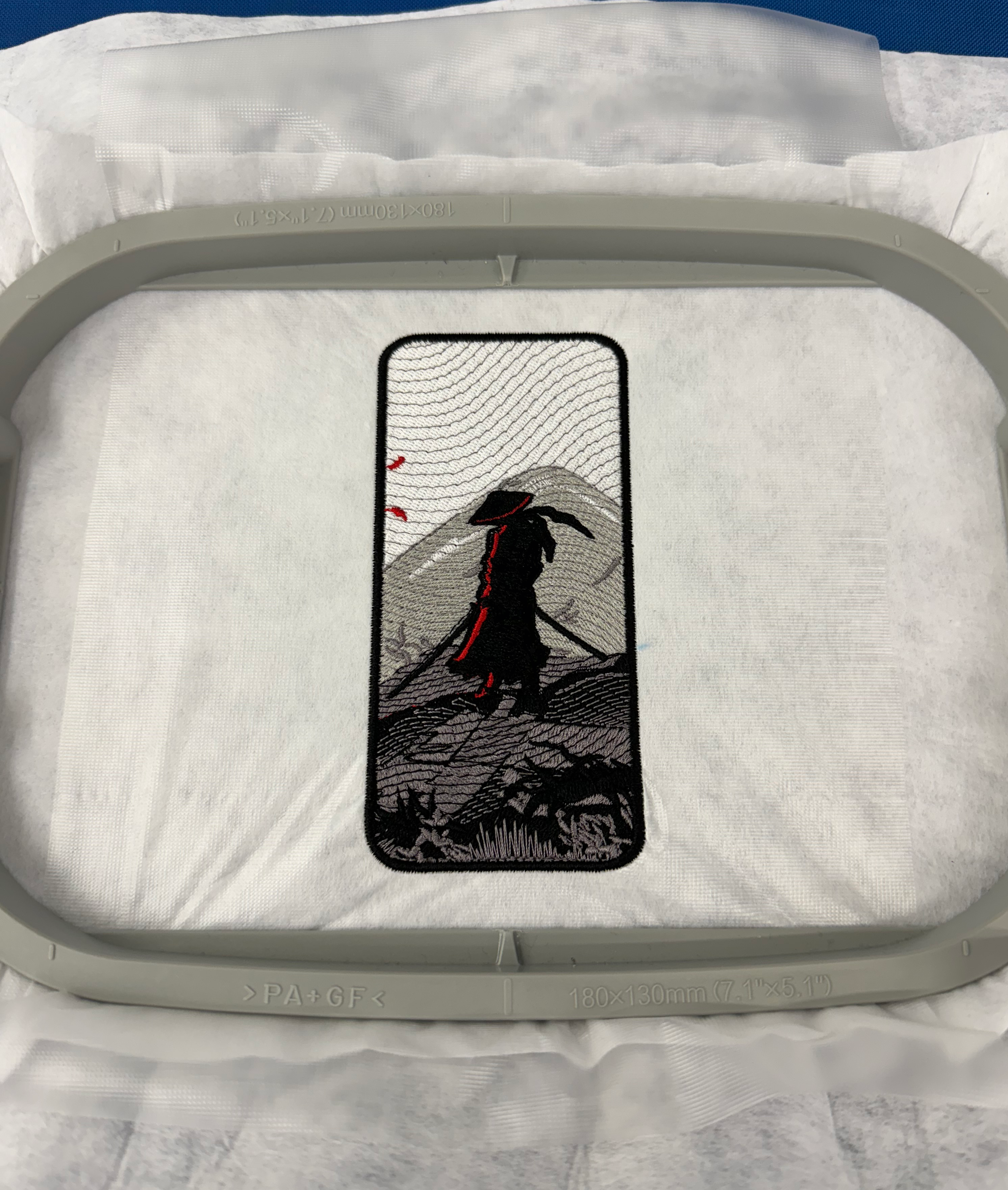 Embroidery hoop with a colorful embroidered design of samurai on a white fabric background